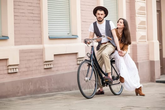 Young couple sitting on a bicycle against the wall in town