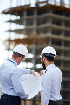 Young architects looking at blueprint with sketch of construction
