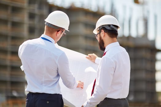 Young architects with blueprint discussing sketch of new building construction