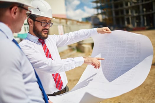 Male architects in helmets discussing blueprint outside