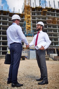Successful young architects handshaking near building structure