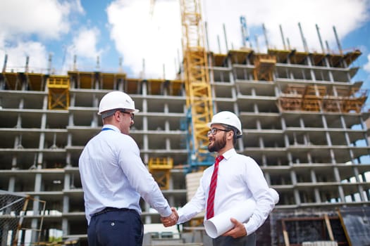Two architects handshaking on background of building structure