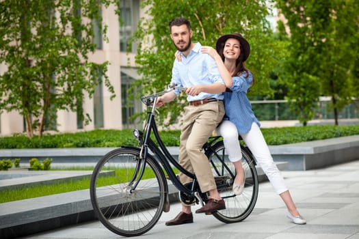Young couple sitting on a bicycle opposite the green city park