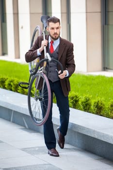 Handsome businessman carrying his bicycle on city streets. The concept of the modern lifestyle of young men