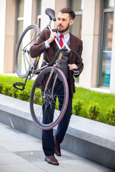 Handsome businessman carrying his bicycle on city streets. The concept of the modern lifestyle of young men