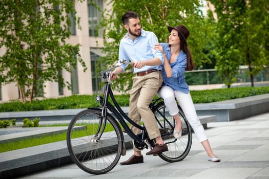 Young couple sitting on a bicycle opposite the green city park