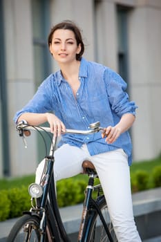 Pretty smiling girl iin blue dress sitting on a bicycle at street