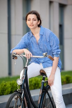 Pretty smiling girl iin blue dress sitting on a bicycle at street
