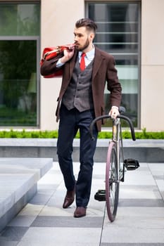 Handsome businessman in a jacket and red tie and his bicycle on city streets. The concept of the modern lifestyle of young men