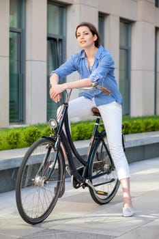 Pretty smiling girl iin blue dress sitting on a bicycle at street