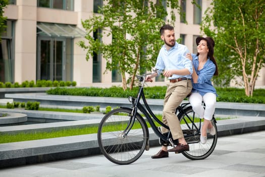 Young couple sitting on a bicycle opposite the green city park