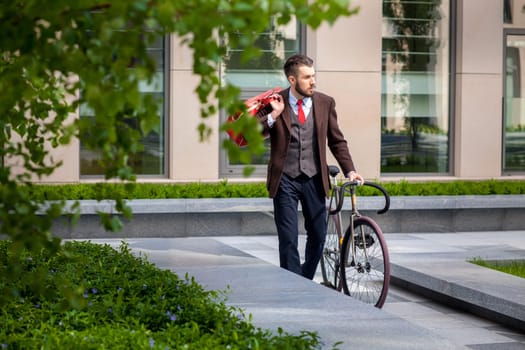 Handsome businessman in a jacket and red tie and his bicycle on city streets. The concept of the modern lifestyle of young men