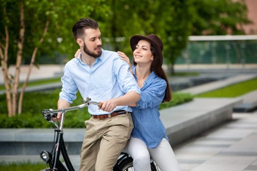 Young couple sitting on a bicycle opposite the green city park
