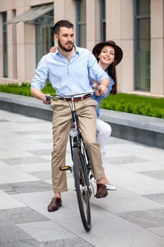 Young couple sitting on a bicycle opposite the green city streets