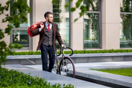 Handsome businessman in a jacket and red tie and his bicycle on city streets. The concept of the modern lifestyle of young men