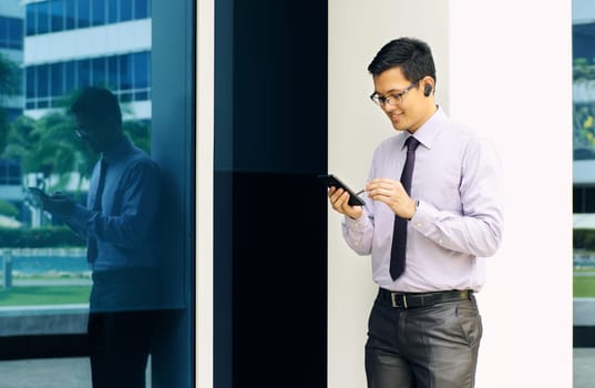 Young chinese businessman typing note on mobile phone while calling with bluetooth headset device. The man uses a digital pen to write on phablet