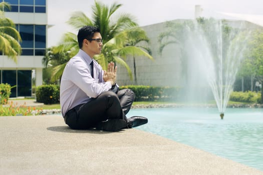 Asian businessman relaxing outside office building. The man does yoga on a bridge and smiles with eyes closed in prayer position
