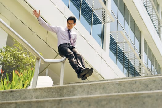 Young and happy chinese businessman sliding downstairs on rails of office staircase. The man enjoys his new promotion at job