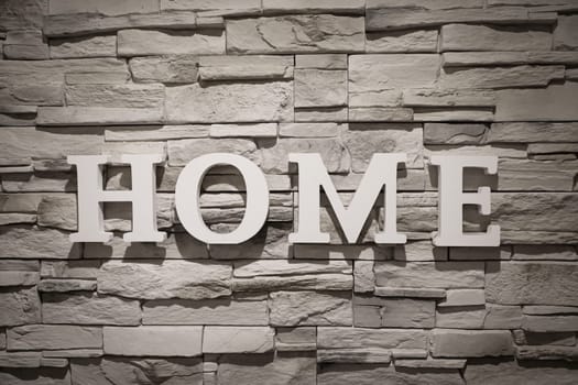 The word "Home"" is written on a wall covered with narrow stones."