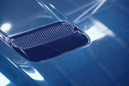front view closeup detail of sport car with blue metal hood and air flow intake ornament