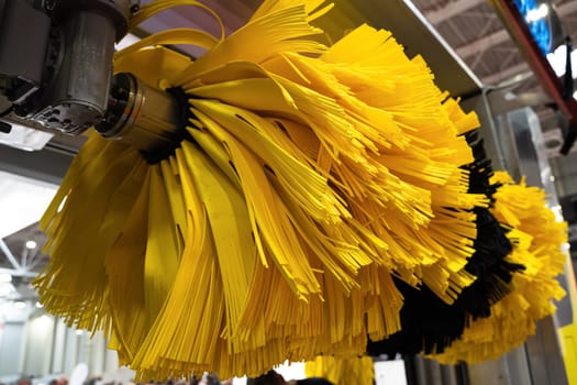 front view closeup detail of black and yellow automatic car wash system cleaning fiber sponge brushes on spinning rotor in an auto service garage station