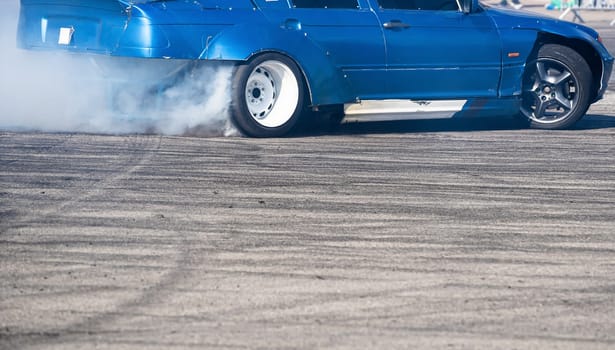 closeup side view of blue sport car drifting on gray speed tarmac track with white smoke coming out of the back tire wheel with copy space available