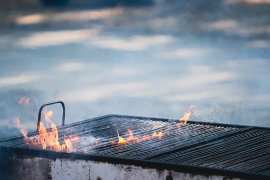 front view closeup detail of metallic large old barbeque grill with fire flames and smoke coming out