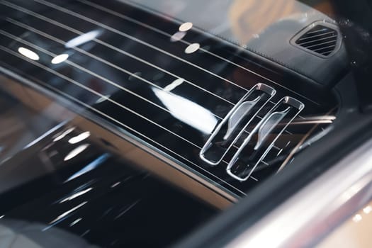 black interior of a luxurious car air conditioning system with leather and shiny chrome dashboard details seen through the side window