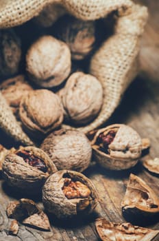 Still life with walnuts and cracked shells in vintage burlap bag. Whole walnut kernel and nutshell on rustic wooden table background.