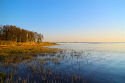 lake autumn landscape, golden hour, yellow forest blue calm smooth water tilt shift