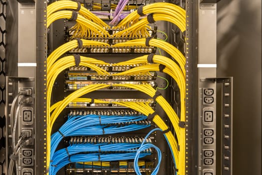 Rack with power sockets on a side, multiple switches and routers with tidily patched network cables, RJ45, data centre, networking