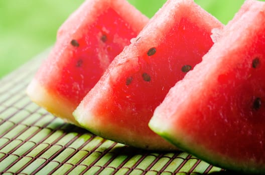 Closeup of sweet red watermelon slices on green table background in garden with sunlight. Summertime refreshing sweet food. Colorful fruit still life..