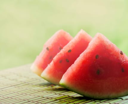 Closeup of sweet red watermelon slices on green table background in garden with sunlight. Summertime refreshing sweet food. Colorful fruit still life.