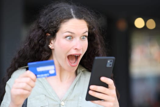 Surprised woman buying online with phone and credit card