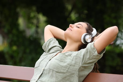 Woman resting listening to music with headphones on a bench in a park