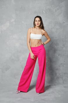 Slender young woman posing in wide cherry pink trousers and white tube top