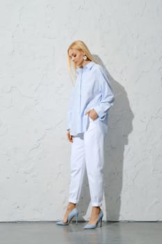 Pensive blonde woman in blue striped shirt, white jeans and stilettos looking down