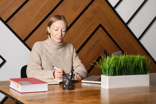 Serious and concentrated adult woman is working hard in co-working and making notes in notepad