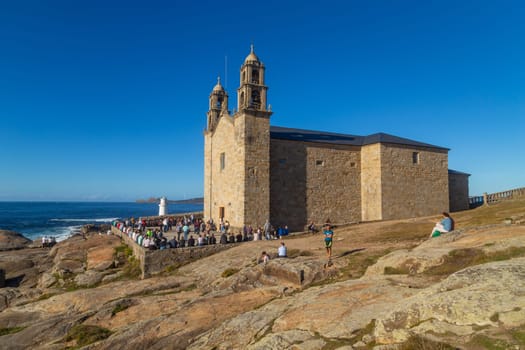 Muxia, A Coruna - Spain August 30, 2022: Virxe de la Barca Sanctuary on Atlantic coast rocks in the foreground afternoon light