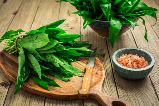 Fresh wild leek leaves on a wooden board. Leaves of fresh ramson with pink Himalayan salt.