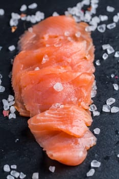Fresh raw salmon fillets. Salmon carpaccio served with salt and lemon on black cutting board.