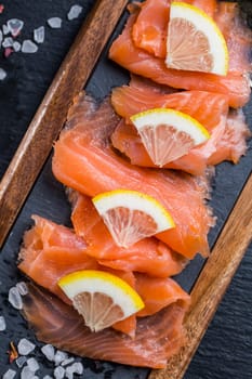 Fresh raw salmon fillets. Salmon carpaccio served with salt and lemon on black cutting board.