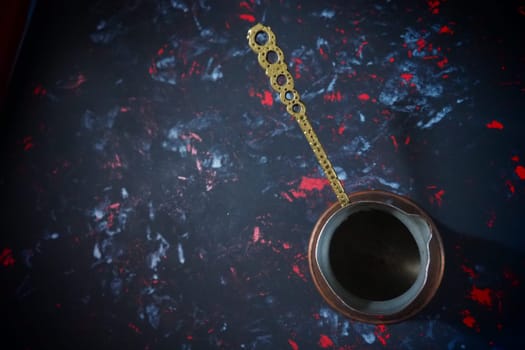 Balkan cezve for turkish coffee. A copper cezve on black surface. Antique bronze utensils. Carved metal handle with pattern. Black background with white, red and blue spots