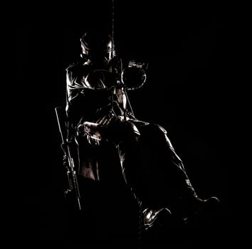 Silhouette of police officer in tactical gear descending from a height, rope exercises with weapons. Tactical rappelling, anti-terror or counter terrorism operation in darkness in rappelling harness