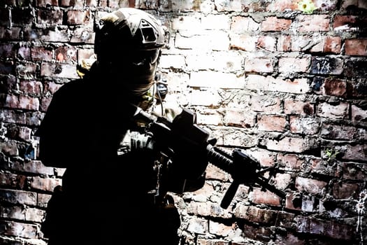 A silhouette of soldier in action in a ruined building, sneaking in darkness along brick wall. Concept of urban military war conflict
