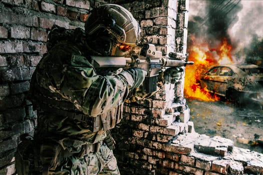 A soldier in action in a ruined building, danger of modern warfare. Fighting in destroyed building, engaged in combat with an unseen enemy. Armed with a firearm and other equipment. Concept of urban military war conflict