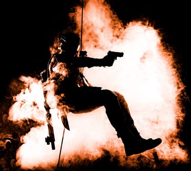 Silhouette of police officer in tactical gear descending from a height, rope exercises with weapons. Tactical rappelling, anti-terror or counter terrorism operation in darkness in rappelling harness