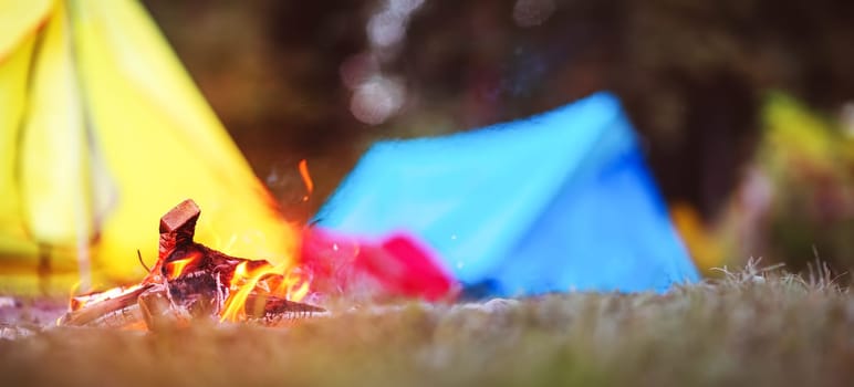 Closeup view of the fireplace near colourful tents in wilderness park. Concept of the camping and active vacation.