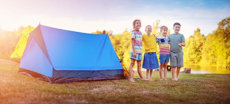 Group of four children standing near colourful tents in nature. Concept of the family vacation, recreation and scouts camping.