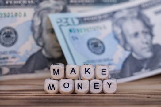The words Make Money, lined with letters on wooden cubes on the background of dollar bills.